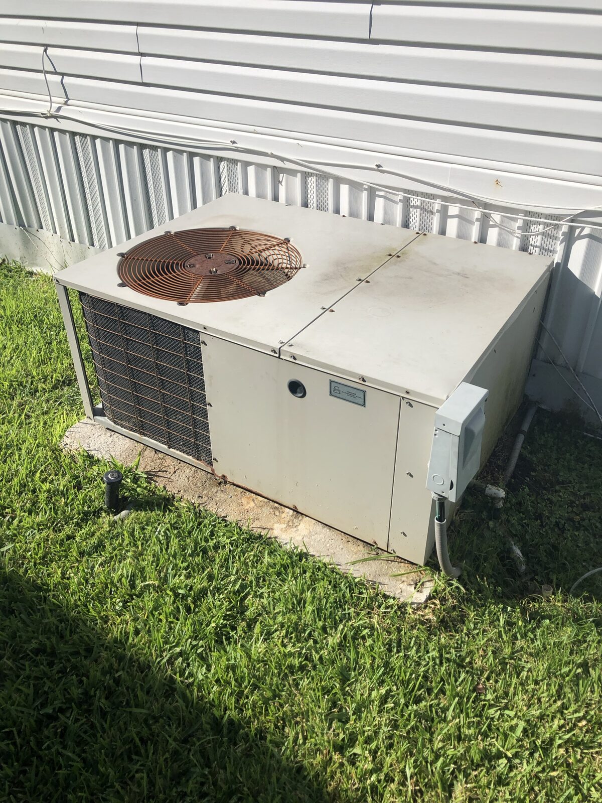 Older residential package HVAC unit beside a house with a rust-streaked top in autumn