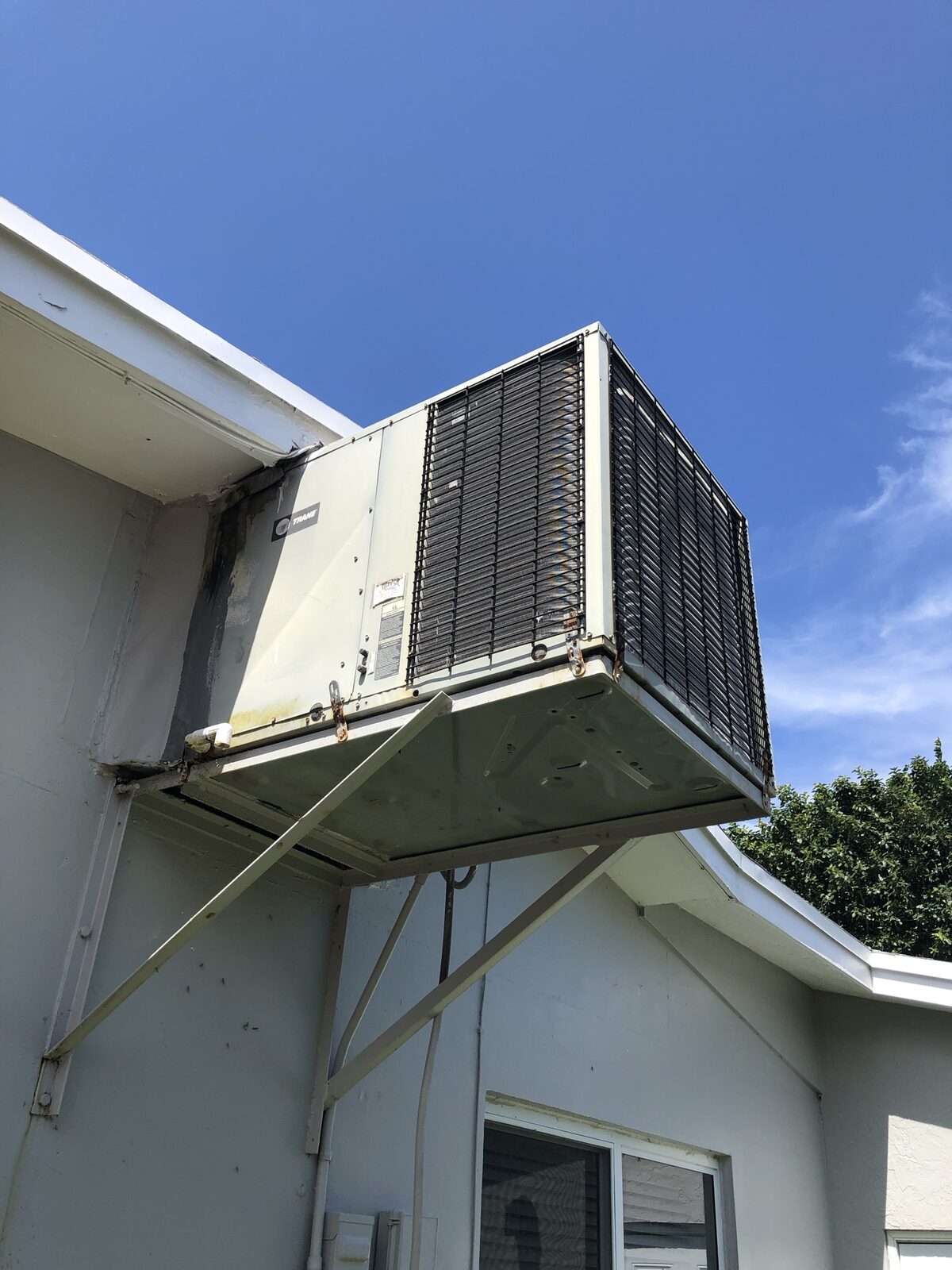 Wall-mounted condenser unit bracketed to the side of a stucco house